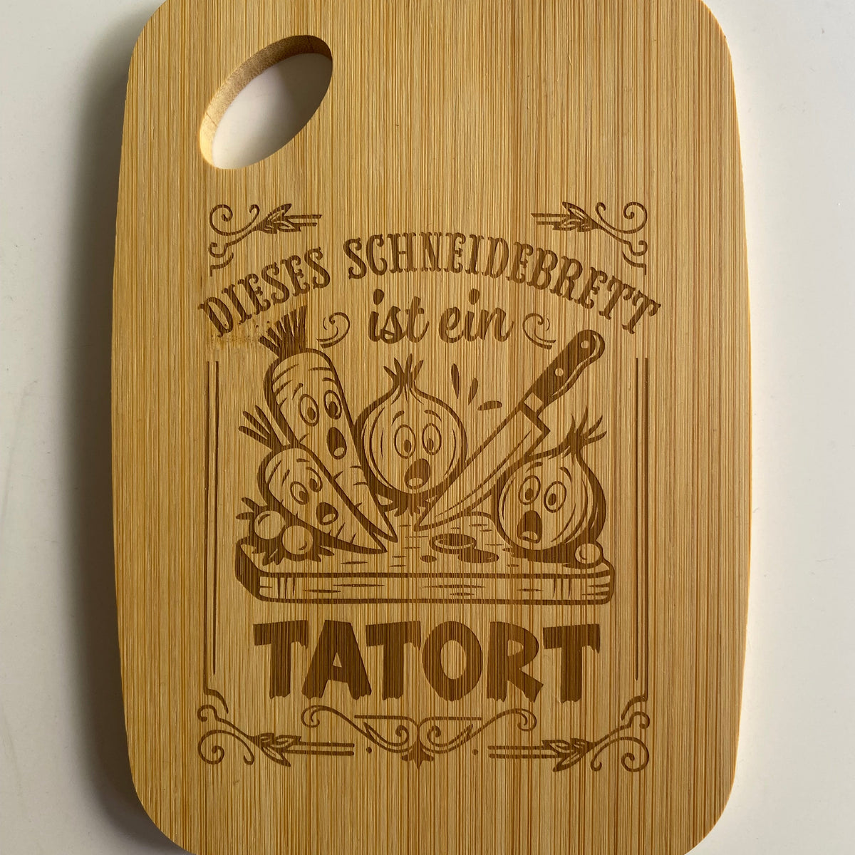 Graviertes Bambus-Schneidebrett mit dem humorvollen Text: „Dieses Schneidebrett ist ein Tatort“ für Hobbyköche.