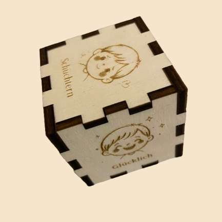 Kleiner Gefühlswürfel aus Holz für Jungen mit den Gravuren Schüchtern und Glücklich vor cremefarbenem Hintergrund.